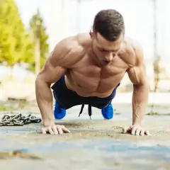 Mięśniowy mężczyzna wykonuje pompki na biceps na zewnątrz. Obok leży ciężki łańcuch.