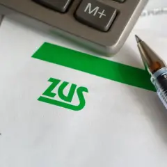 Długopis i kalkulator leżą na papierze z logo ZUS. Czas na rozliczenie składek społecznych.