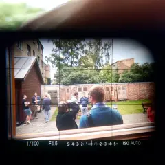 Obraz widoczny w wizjerze kamery: grupa ludzi na podwórku, jeden z nich robi zdjęcie.