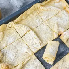 Frisch gebackener Ofenpfannkuchen, in Quadrate geschnitten und mit Puderzucker bestäubt. Ein einzelnes Stück ist aufgerollt und zeigt die Füllung.
