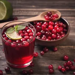 Orzeźwiający sok żurawinowy z plasterkiem limonki i miętą, obok miseczka pełna owoców.