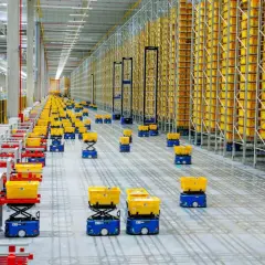 Nowoczesny hub logistyczny z autonomicznymi robotami przewożącymi żółte kosze pośród wysokich regałów wypełnionych towarami.