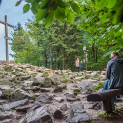 Kamienista ścieżka prowadzi do wejścia na Łysicę, gdzie widać drewniany krzyż i odpoczywających turystów.