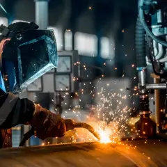 Spawacz w masce ochronnej używa elektrod do aluminium, tworząc iskry podczas pracy przy metalowej konstrukcji.