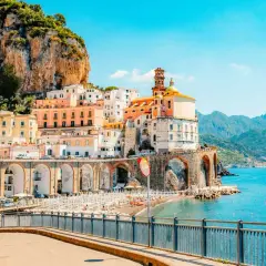 Colorful buildings cling to a cliffside overlooking a beach and the turquoise sea, a quintessential view of Amalfi Coast cities.