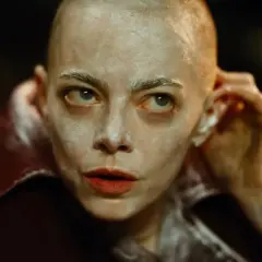 Kobieta z ogoloną głową i białym makijażem, w czerwonym płaszczu, wygląda jak postać z filmów o porwaniach.