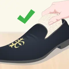 Une main insère un embauchoir dans une chaussure de ville noire ornée d'un motif doré. La mise en forme des chaussures est essentielle pour leur longévité. ✅