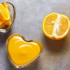 Arance fresche, spicchi e succo in ciotole a forma di cuore. Scopri quale alimento contiene più vitamina C per un cuore sano!