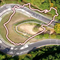 Widok z lotu ptaka na fragment toru Nürburgring otoczony lasem. Czerwona linia obrysowuje trasę, ukazując jej kręty kształt.