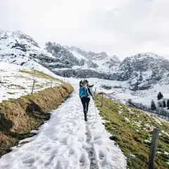 Une randonnée ce week-end dans un paysage montagneux enneigé. Des randonneurs suivent un sentier bordé de clôtures en bois, avec des sommets imposants en arrière-plan.
