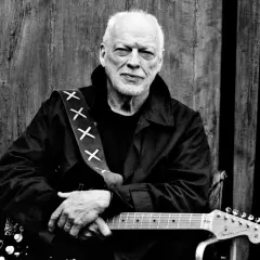 David Gilmour z najdroższą gitarą na świecie, oparty o drewniane drzwi.