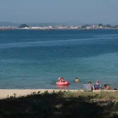 Gente disfruta de un día soleado en las playas de O Grove, con niños jugando en el agua y adultos relajándose en la arena.