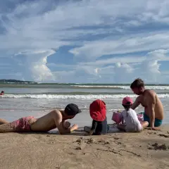 Familj njuter av en solig dag på stranden i Sri Lanka. En man ligger i sanden medan en annan leker med barnen vid havet.