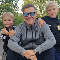 Marcin Mroczek z uśmiechem i dwoma synami, którzy go obejmują. Radosny dzień ojca i dzieci.