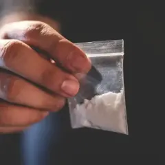 Dłoń trzymająca małą, przezroczystą torebkę z białym proszkiem.