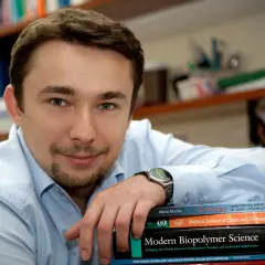 Mężczyzna w jasnej koszuli opiera rękę na stosie książek, w tym na tej zatytułowanej "Chitozan".