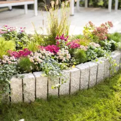 Ein Blumenbeet mit typischen Gartenpflanzen wie Astern und Gräsern, umrahmt von Granitsteinen. Efeu rankt über die Steine.