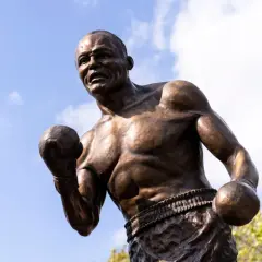 Bronze statue of boxer Jersey Joe Walcott in a fighting stance against a blue sky with clouds.