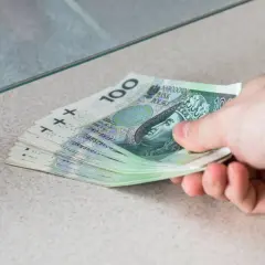 Dłoń przekazuje stos banknotów 100 zł. To przykład, co to depozyt bankowy – pieniądze wpłacane do banku.