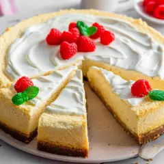 Ein New York Cheesecake, dekoriert mit frischen Himbeeren und Minze, wartet darauf, genossen zu werden.