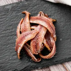 Na czarnej desce ułożone są fileciki anchois. To małe, słone rybki, idealne do sałatek i sosów.
