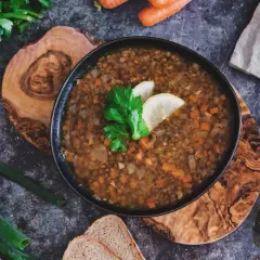 Herzhafte italienische Linsensuppe mit Karotten und Sellerie, garniert mit Zitrone und Petersilie, daneben Brot und frische Kräuter.