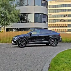 Elegancki, czarny Renault Arkana na tle nowoczesnych budynków. Zwróć uwagę na jego dynamiczne linie, które podkreślają jego sportowy charakter i optymalne renault arkana wymiary.