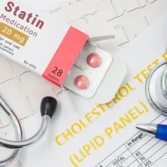 Lekarz bada wyniki cholesterolu, obok leży stetoskop i opakowanie leku Statin 20 mg.