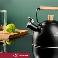 Czajnik Gerlach z drewnianym uchwytem, gotowy do zaparzenia aromatycznej kawy w garnku. Obok szklanka z herbatą i świeże owoce.