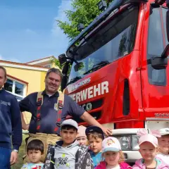 Feuerwehrleute und Kinder vor einem roten Feuerwehrauto. Ein fröhlicher Tag der Feuerwehr!
