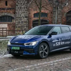Niebieska Kia EV6 z napisem "#GOelectric D do 528 km zasięgu" stoi przed zabytkową ceglaną budowlą.
