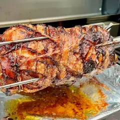 Ein saftiges, am Spieß gebratenes Stück Fleisch, das nach Porchetta aussieht, tropft in eine Aluschale.