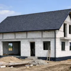 Dom w budowie z betonu komórkowego, najtańszy materiał na budowę domu. Dach pokryty ciemną dachówką, okna i drzwi jeszcze nie zamontowane.
