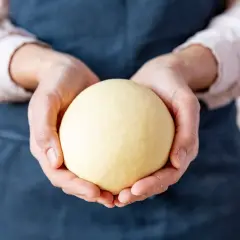 Hände halten einen glatten, gelben Ball aus nudelteig ohne ei.