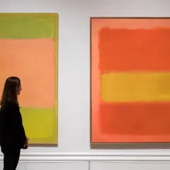 Kobieta podziwia abstrakcyjne dzieła sztuki obrazy Rothko: zielono-pomarańczowy i pomarańczowo-żółty.