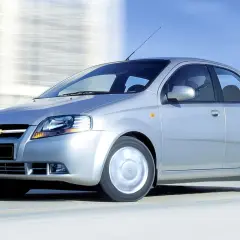 Srebrny Chevrolet Kalos, model Aveo, pędzi po drodze, rozmywając tło.