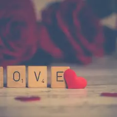 Lettere di legno formano la parola "LOVE" su uno sfondo di rose rosse, evocando le più belle canzoni dolci italiane.
