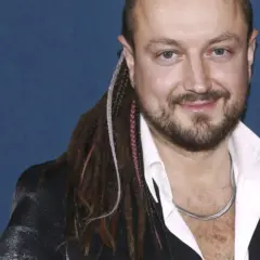 Aleksander Milwiw-Baron, znany z charakterystycznych dredów, z uśmiechem na twarzy. Jego pochodzenie jest często tematem dyskusji.