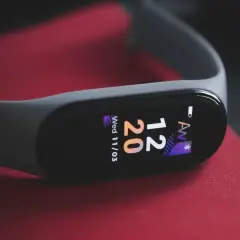 Szary smartband do pływania na czerwonym tle. Wyświetla godzinę 12:20 i datę.