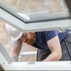 Handwerker mit Bart und Helm dichtet provisorisch das Dach ab.