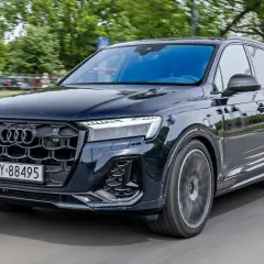 Elegancki, ciemny Audi Q7 2026 pędzi po drodze, otoczony zielenią.