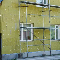 Lavori in corso per pulire muro esterno con cappotto isolante. L'edificio è circondato da ponteggi metallici.