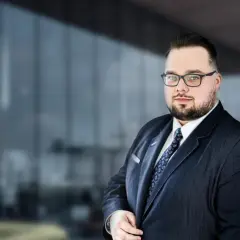 Mężczyzna w garniturze i okularach na tle nowoczesnego budynku.
