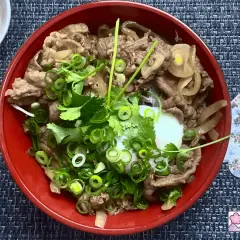 A delicious wagyu donburi with thinly sliced beef, onions, and a perfectly poached egg, garnished with fresh scallions and cilantro.