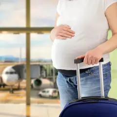 Ciężarna kobieta z walizką na lotnisku, gotowa do podróży. Wygląda na to, że jest fit to fly.