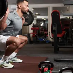 Mężczyzna wykonuje przysiad ze sztangą, napinając mięśnie brzucha, co jest kluczowe dla techniki manewr Valsalvy.