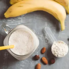 Ein cremiger Proteinshake mit Banane und Nüssen, daneben eine Schaufel Proteinpulver, bereit für das Training. Kreatin im Proteinshake für mehr Power.