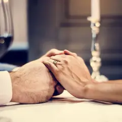 Dłonie splecione na stole, pierścionek na palcu. Romantyczna kolacja, idealna na życzenia na rocznicę ślubu dla męża.