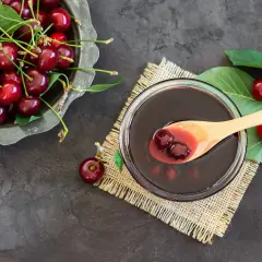 Miseczka pełna soczystych wiśni obok szklanej miseczki z gęstą, ciemnoczerwoną frużeliną wiśniową. Drewniana łyżka zanurzona w słodkiej masie.