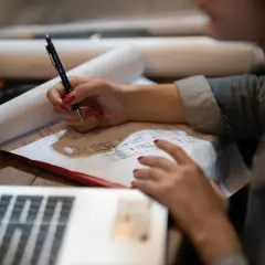 Rysunek techniczny, przypominający przykładowy wypis z rejestru gruntów, na którym osoba z czerwonymi paznokciami pisze długopisem.